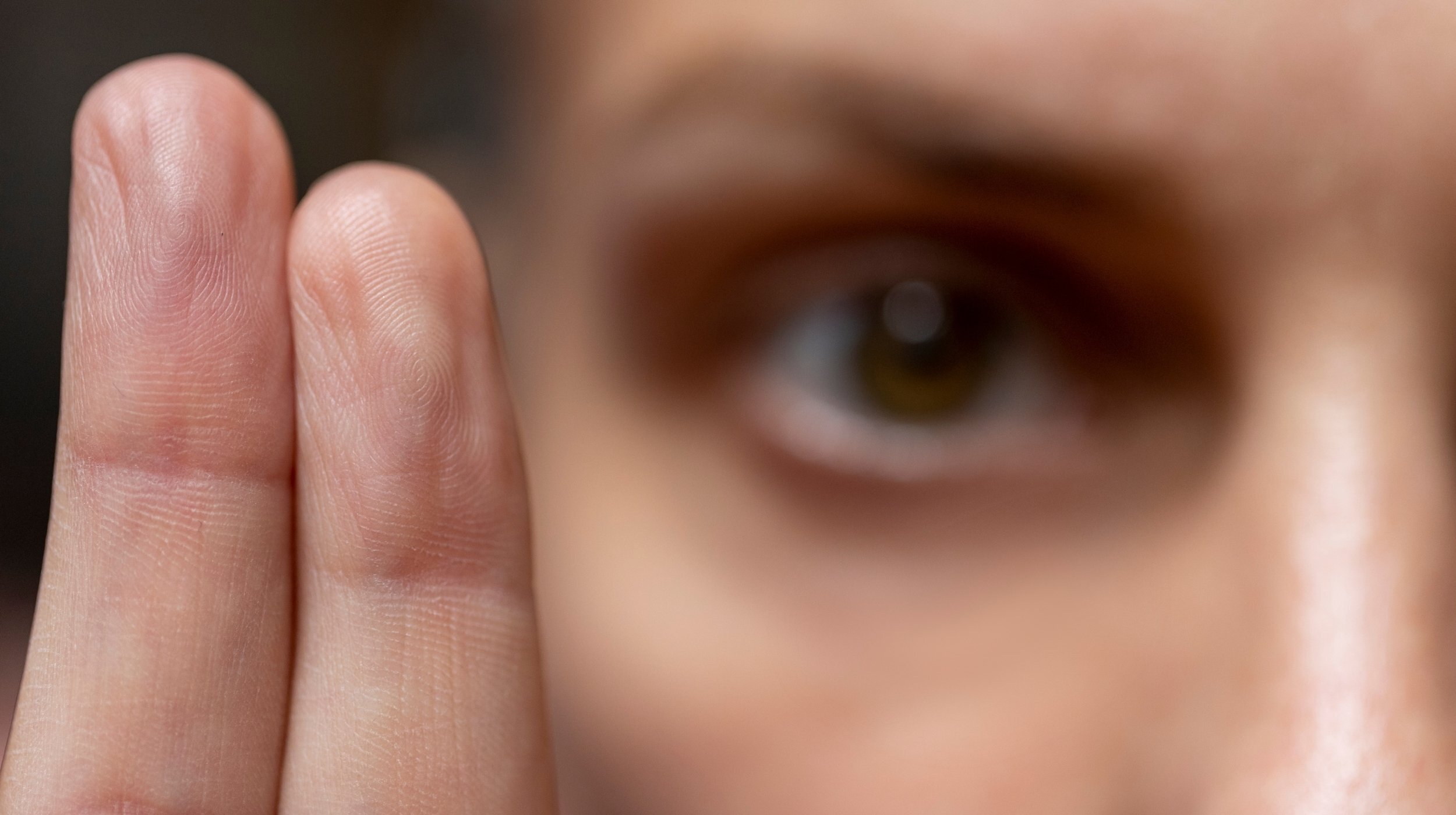 Close-up of a person’s face with their hand raised in the foreground, showing a focused and attentive expression.